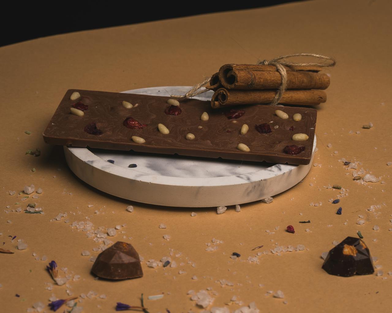 Delicious chocolate bar with nuts and berries on a marble plate, garnished with cinnamon sticks.